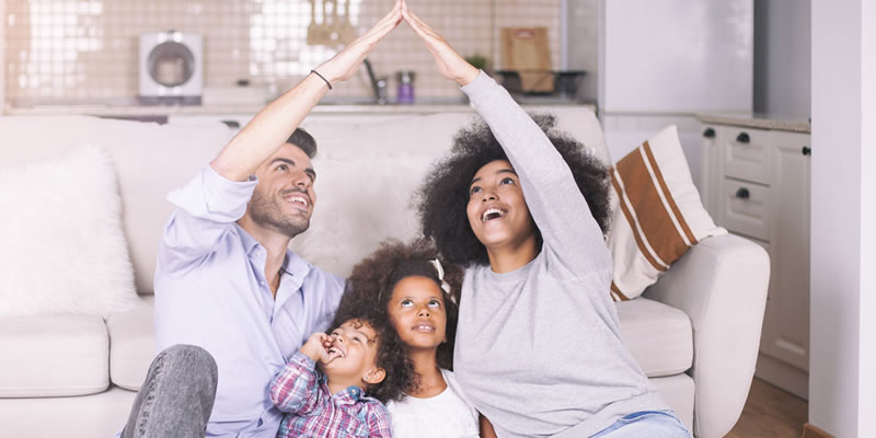 Father, mother and children smiling and sitting on a couch. Sandy Spring Insurance Personal Umbrella Liability Insurance.