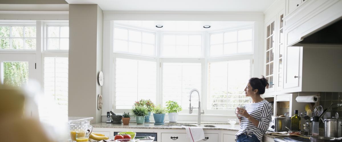 A woman drinking coffee in a bright new kitchen with large windows. A home equity loan can help your home improvement dreams become real. Sandy Spring Bank Home Equity Loans.