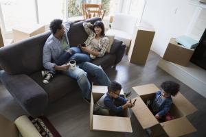 Couple sitting on couch as their children play in boxes after they have moved into their new house. Sandy Spring Bank Mortgages.