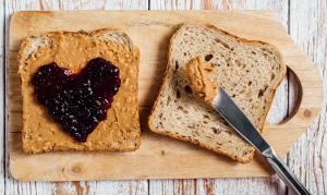 A cutting board with two slices of wheat bread. One piece has peanut with on jeally in the shape of a heart on top of the peanut butter. Sandy Spring Bank